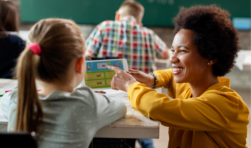 teacher with female student in classroom playing reading eggs on ipad